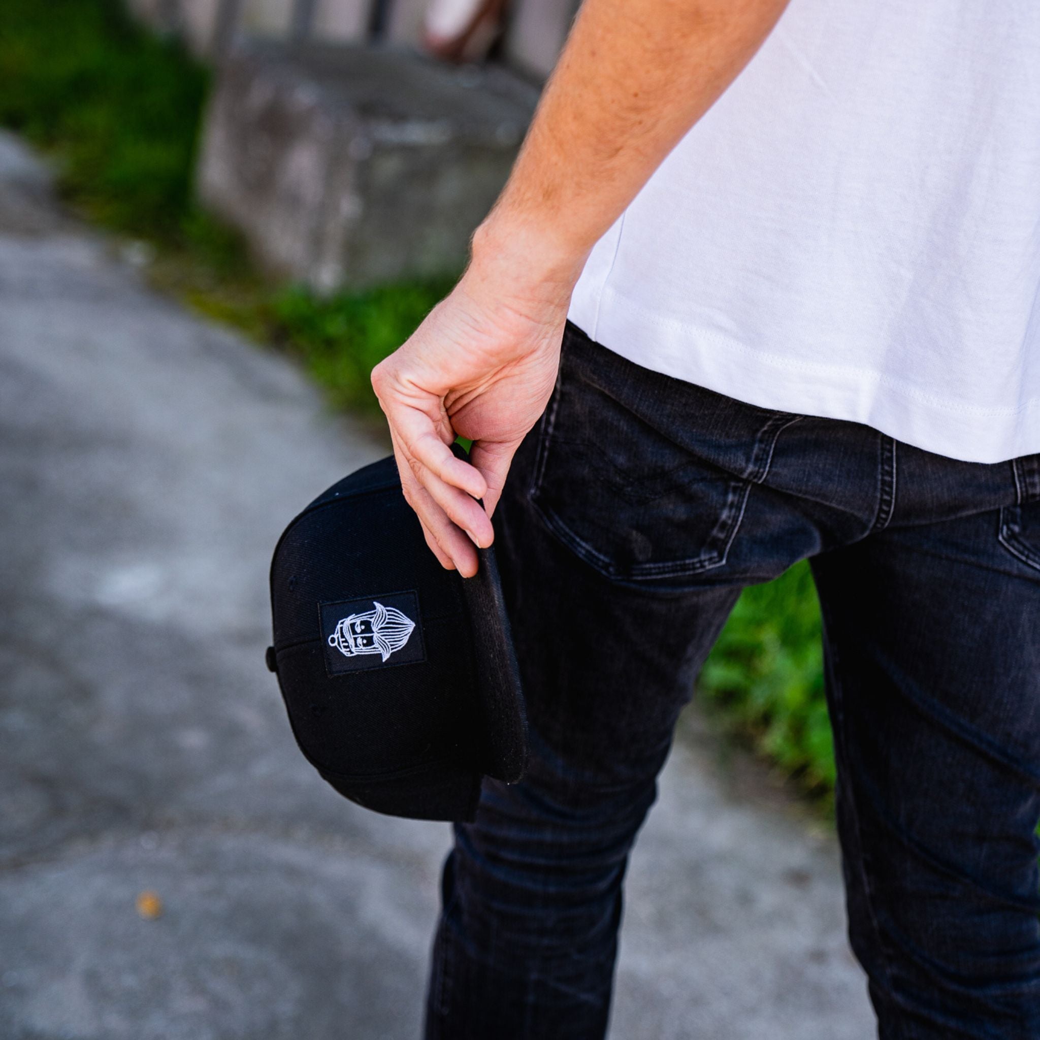 Person hält schwarze Fangfrisch Cap mit Matrosen Logo in der Hand beim Gehen