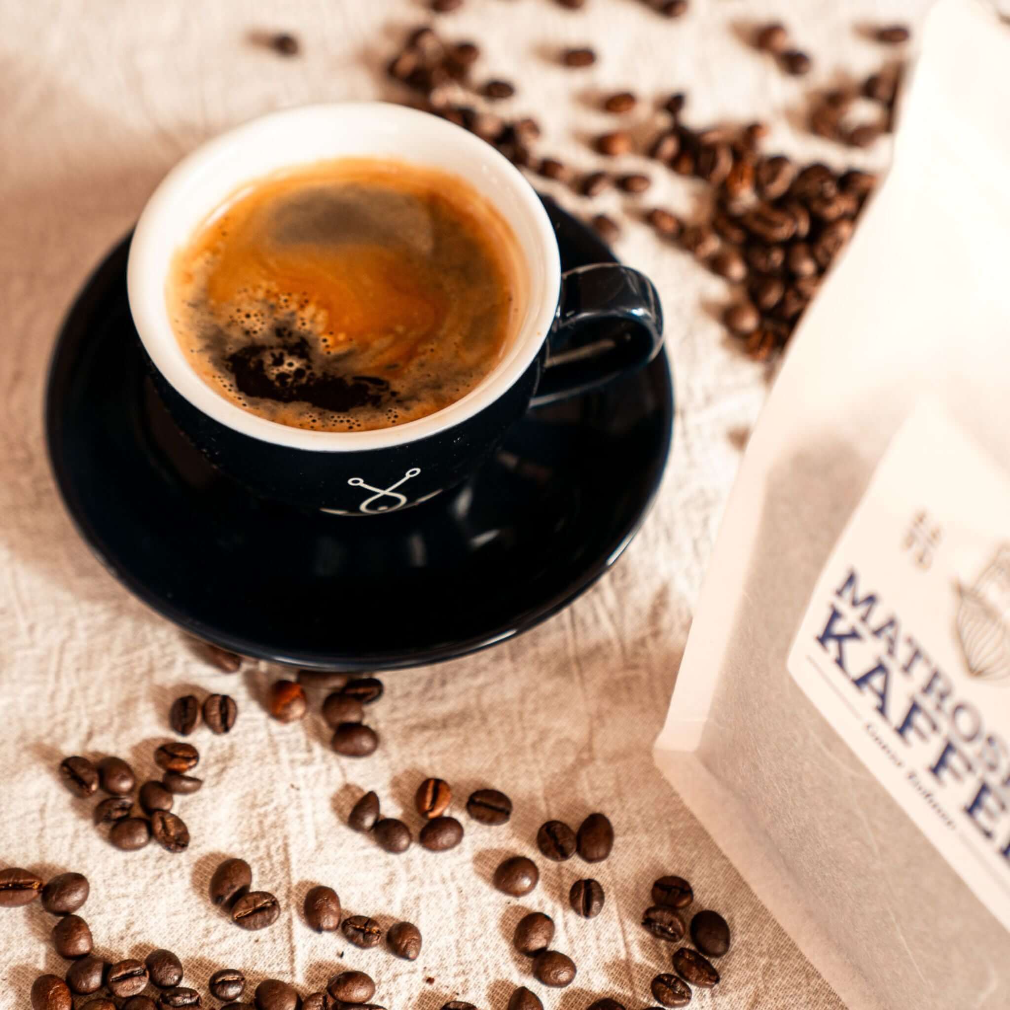 Dunkelblaue Cappuccino Tasse mit Kaffeebohnen – Fangfrisch