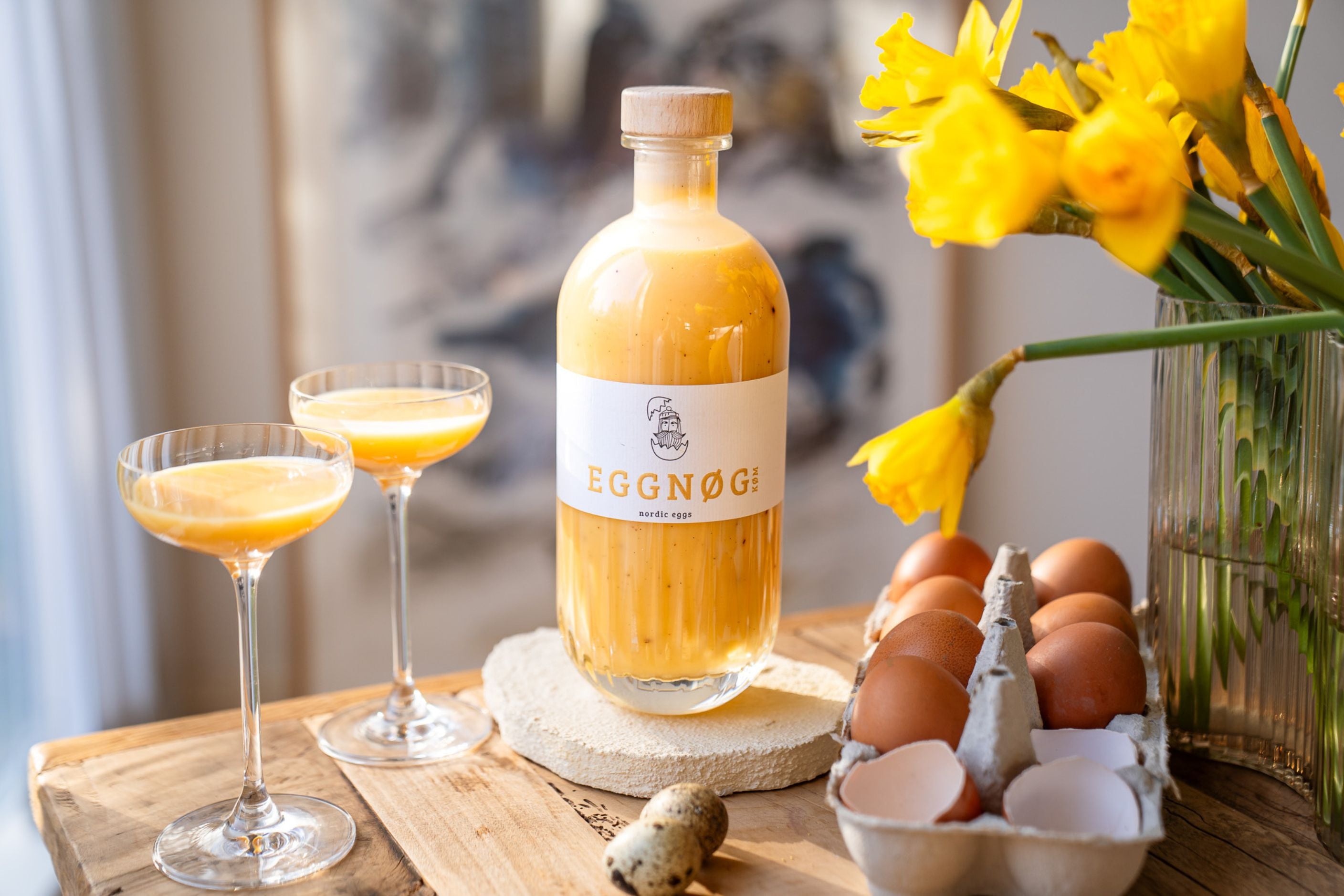Flasche Eierlikör mit zwei Gläsern und Eiern auf Holztisch