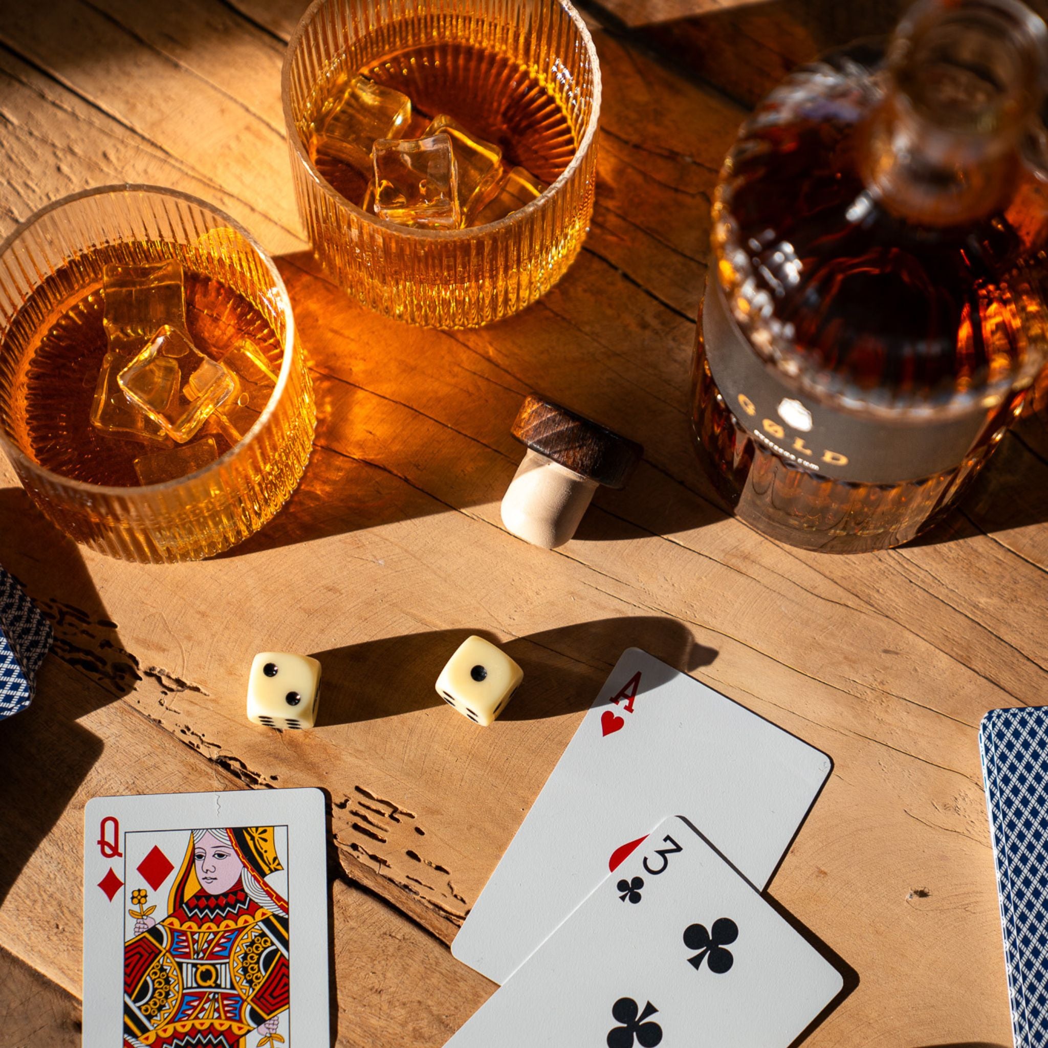 Inszenierte Glücksspielszene mit GØLD Overseas Rum Flasche und Rumgläsern mit Eiswürfeln