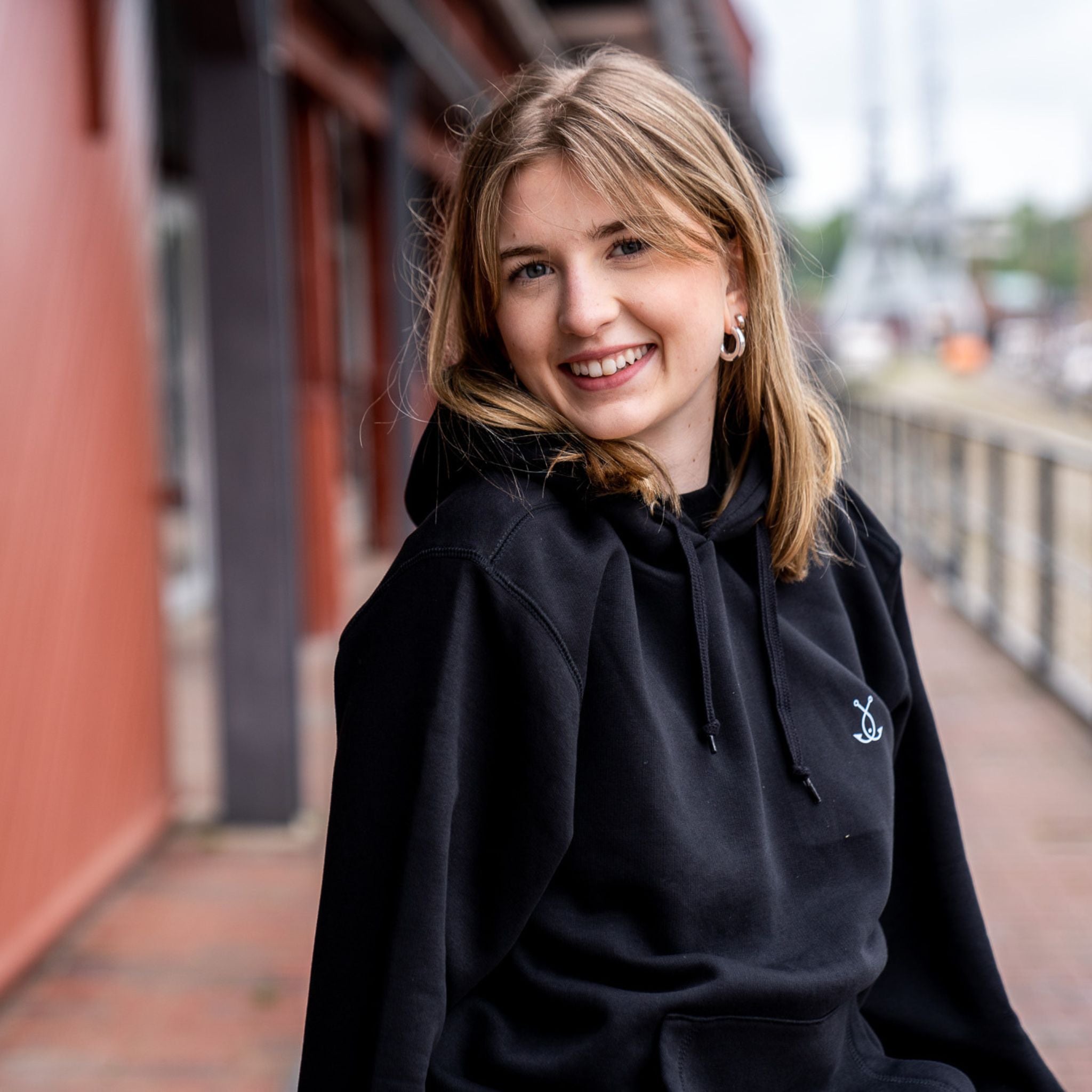 Frau trägt schwarzen Fangfrisch Hoodie am Hafengebäude
