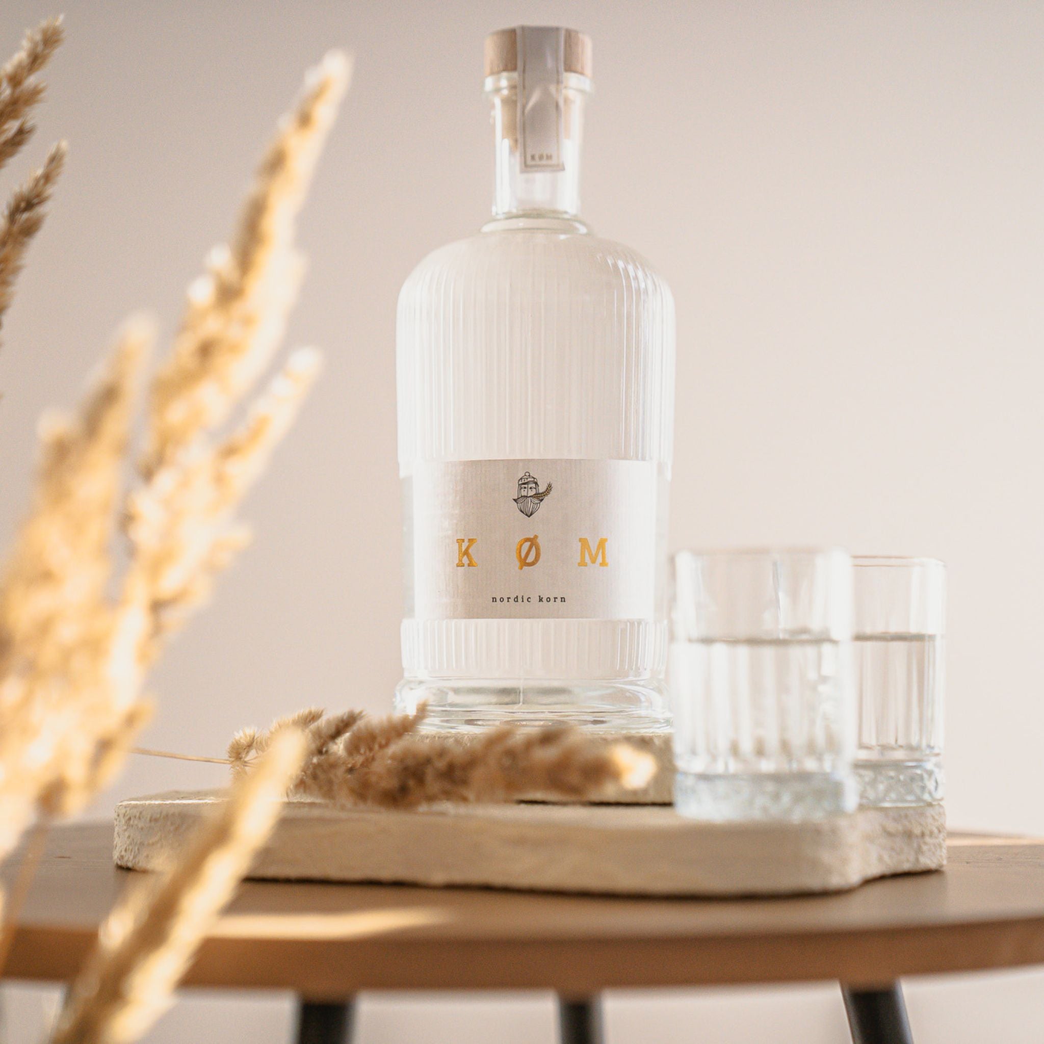 KØM Nordic Korn Flasche auf Holztablett mit zwei Gläsern im warmen Licht