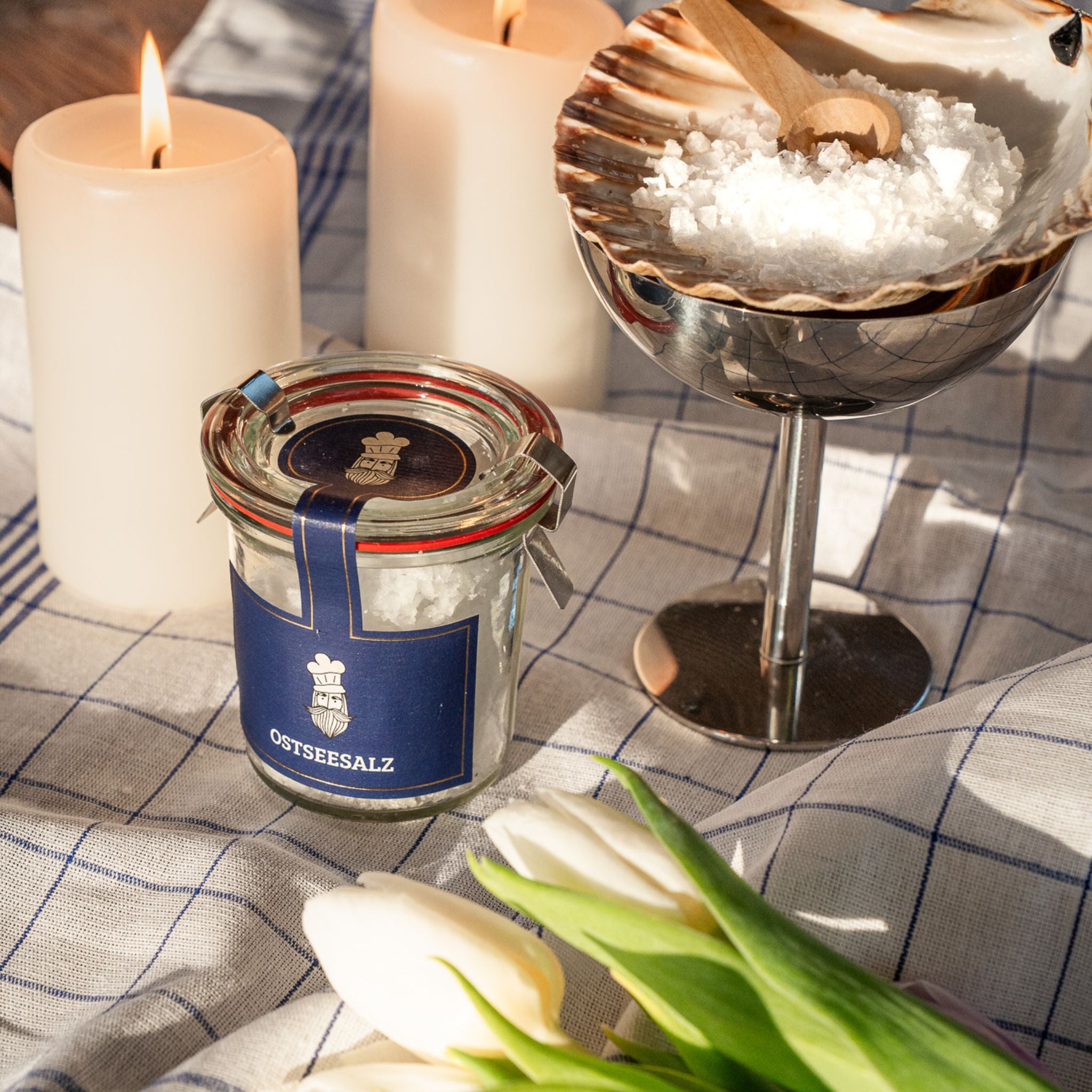Glas mit Ostseesalz auf einem Tisch, umgeben von Kerzen und frischen Tulpen.