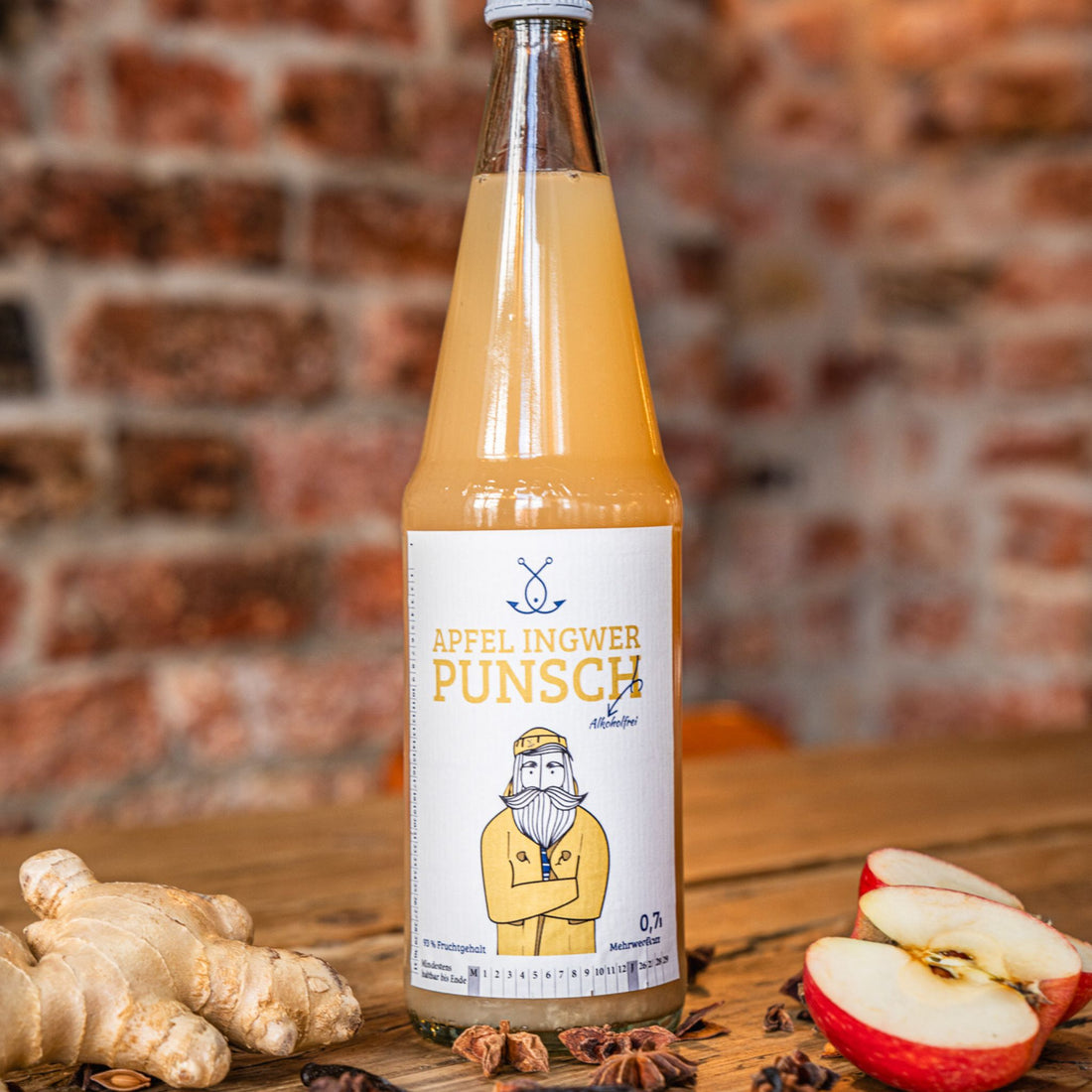 Flasche Apfel Ingwer Punsch auf Holztisch mit Äpfeln und Gewürzen
