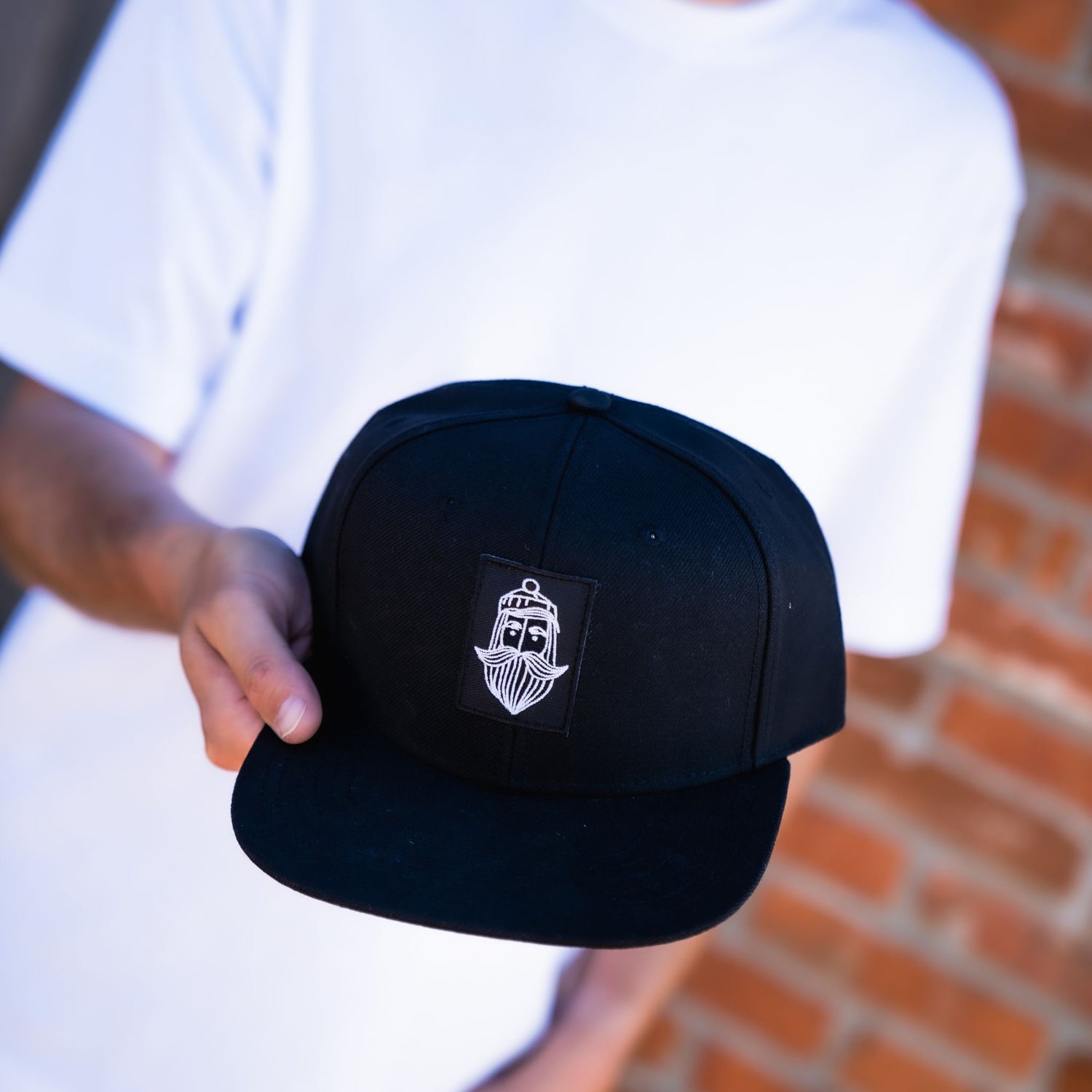 Fangfrisch Cap schwarz mit Matrosen Logo in der Hand gehalten vor Ziegelwand