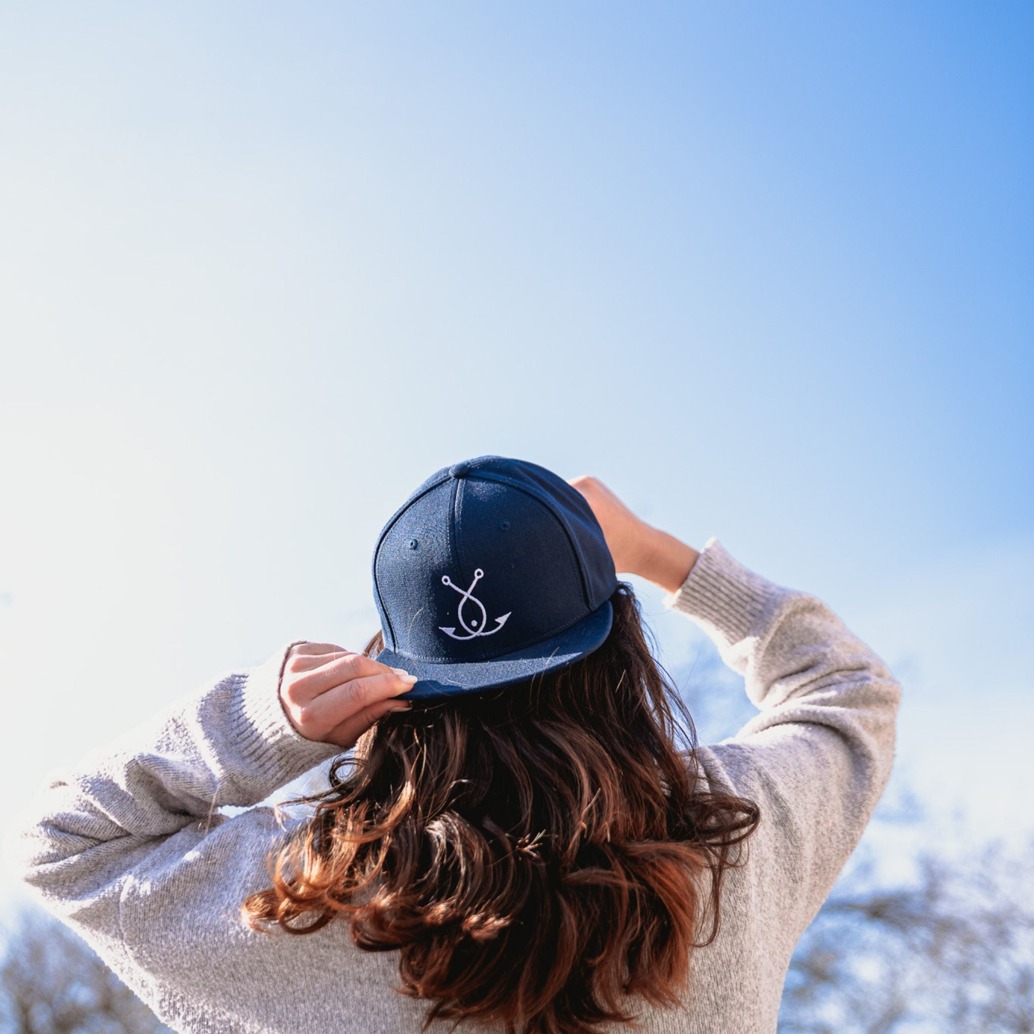 Person trägt blaue Fangfrisch Cap mit Anker Logo vor Bergkulisse