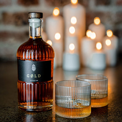 GØLD Overseas Rum und zwei gefüllte Rumgläser mit Kerzen im Hintergrund