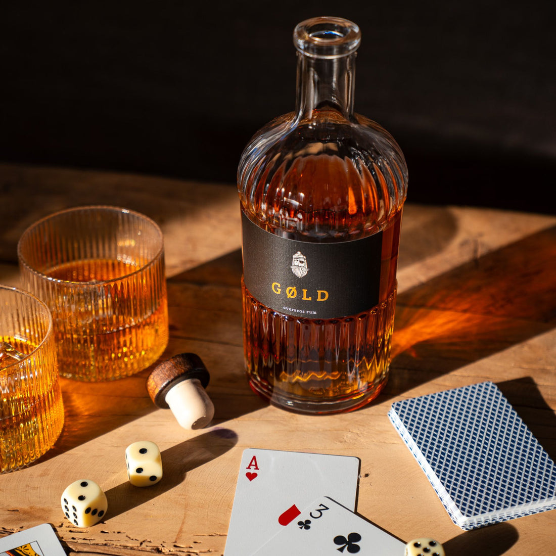 Inszenierte Glücksspielszene mit GØLD Overseas Rum Flasche und Rumgläsern mit Eiswürfeln