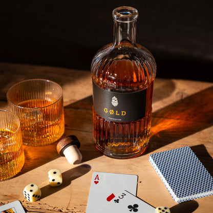 Inszenierte Glücksspielszene mit GØLD Overseas Rum Flasche und Rumgläsern mit Eiswürfeln