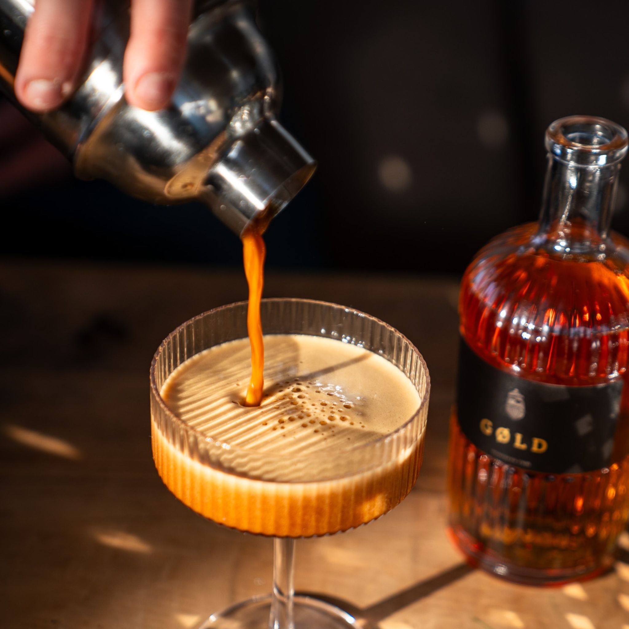 Espresso Martini wird in ein Cocktail Glas eingeschenkt neben einer GØLD Overseas Rum Flasche 
