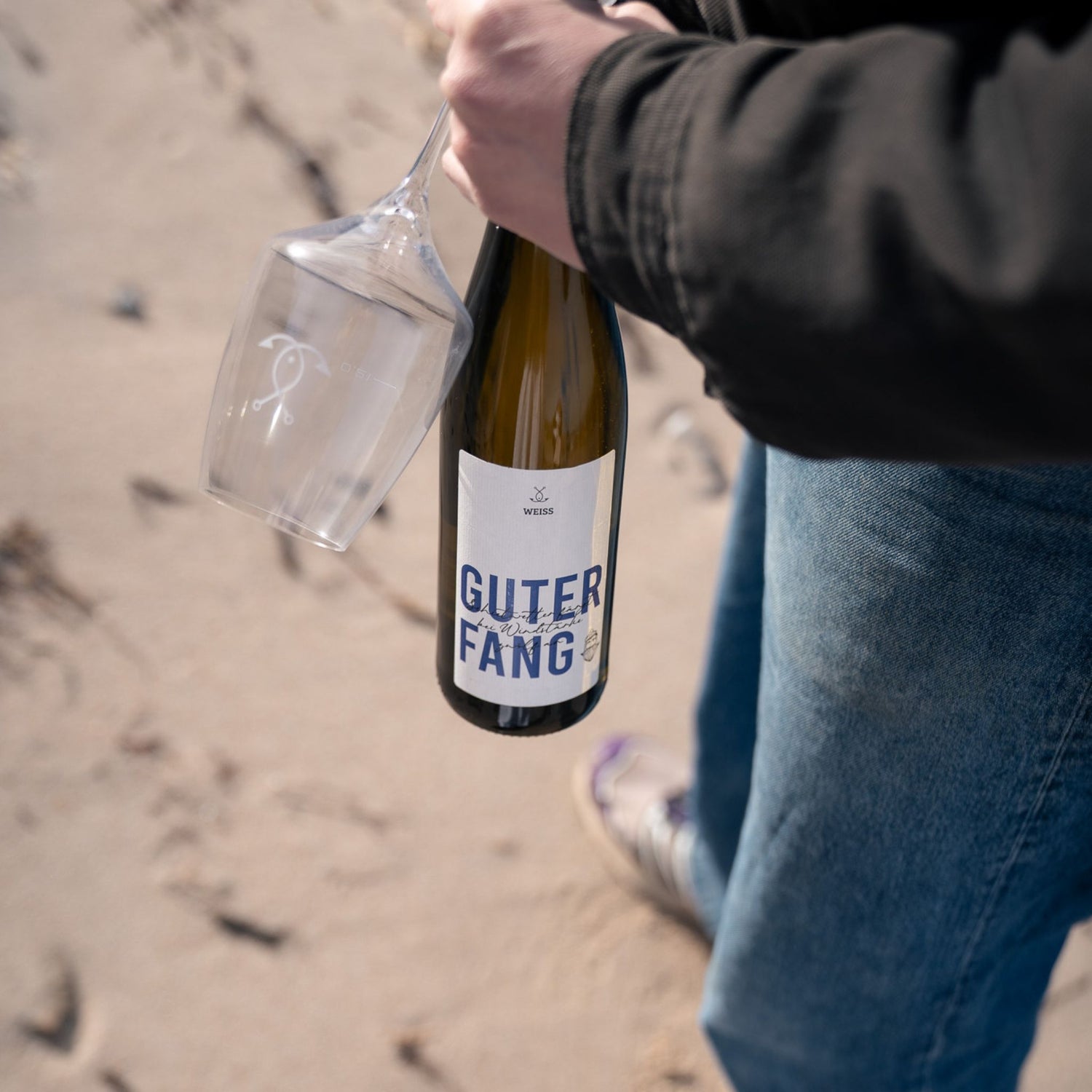 Weißweinflasche Guter Fang Weiß  in der Hand am Strand