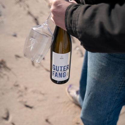 Weißweinflasche Guter Fang Weiß  in der Hand am Strand