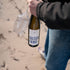 Weißweinflasche Guter Fang Weiß  in der Hand am Strand