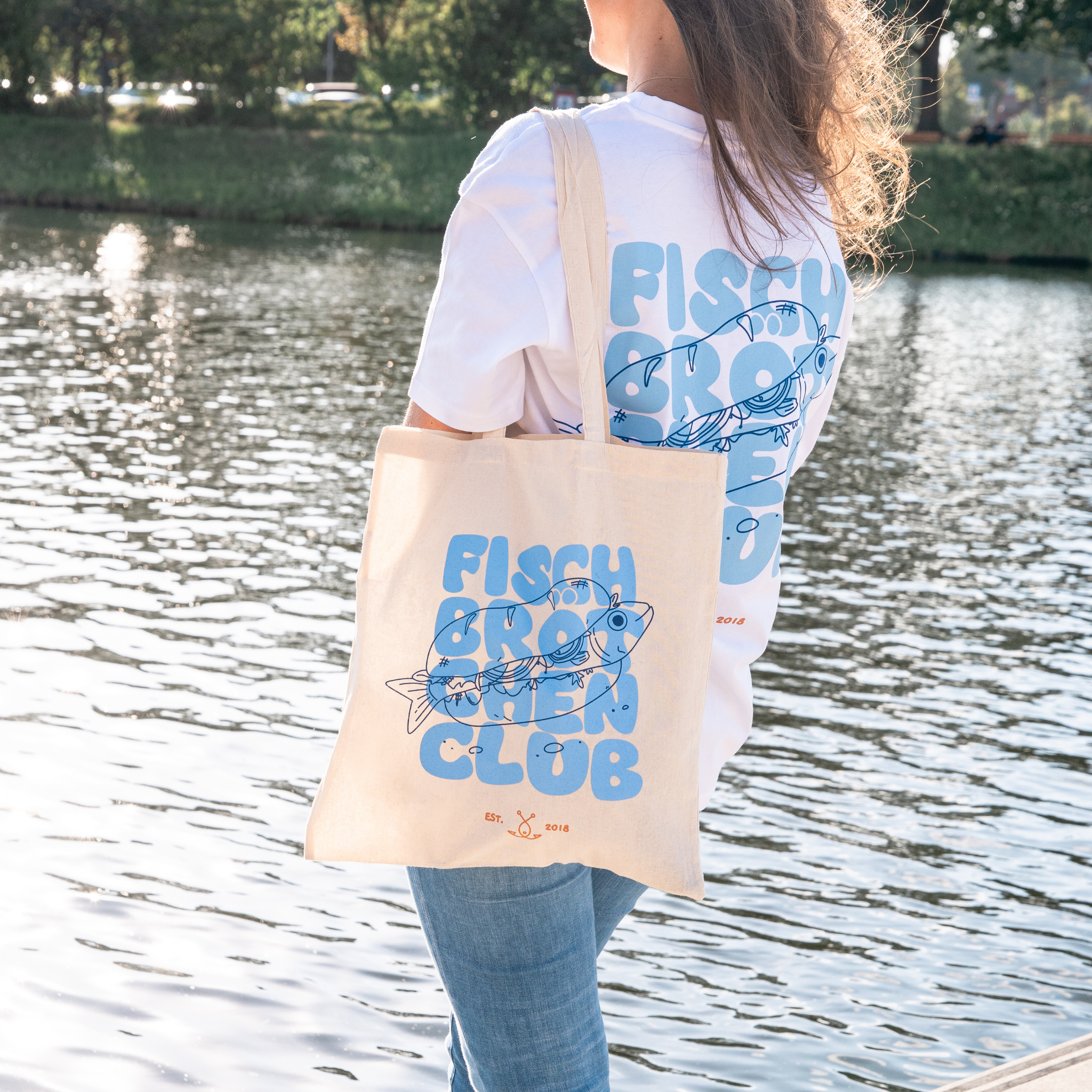 Frau trägt Fischbrötchenclub Jutebeutel über der Schulter am Wasser in Lübeck