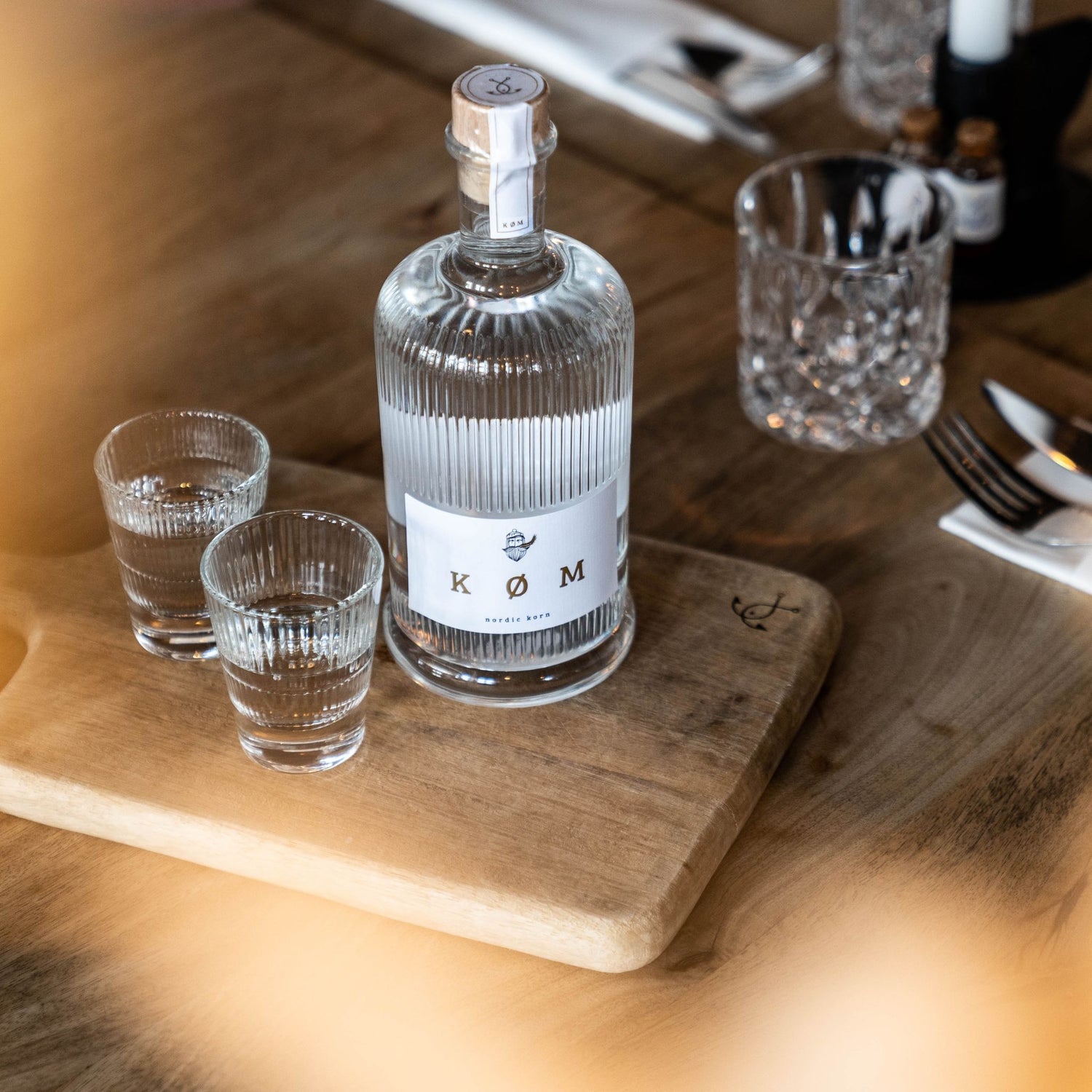 Flasche KØM Nordic Korn auf Holzbrett mit zwei Gläsern in stilvollem Ambiente
