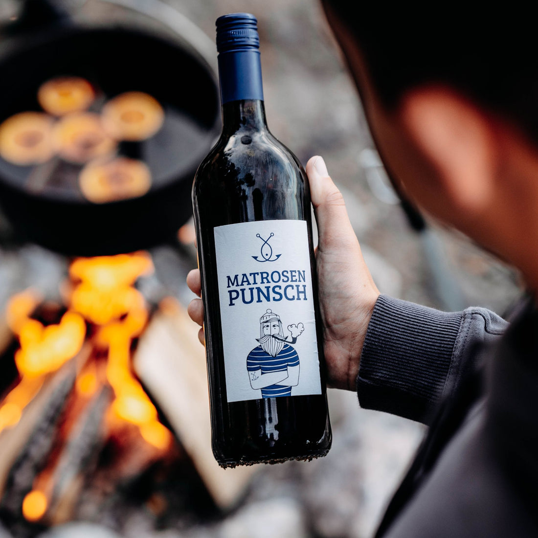Hand hält große Flasche Matrosenpunsch vor Lagerfeuer, Outdoor Glühwein Szene