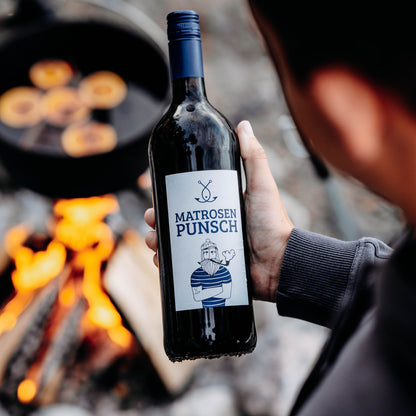 Hand hält große Flasche Matrosenpunsch vor Lagerfeuer, Outdoor Glühwein Szene