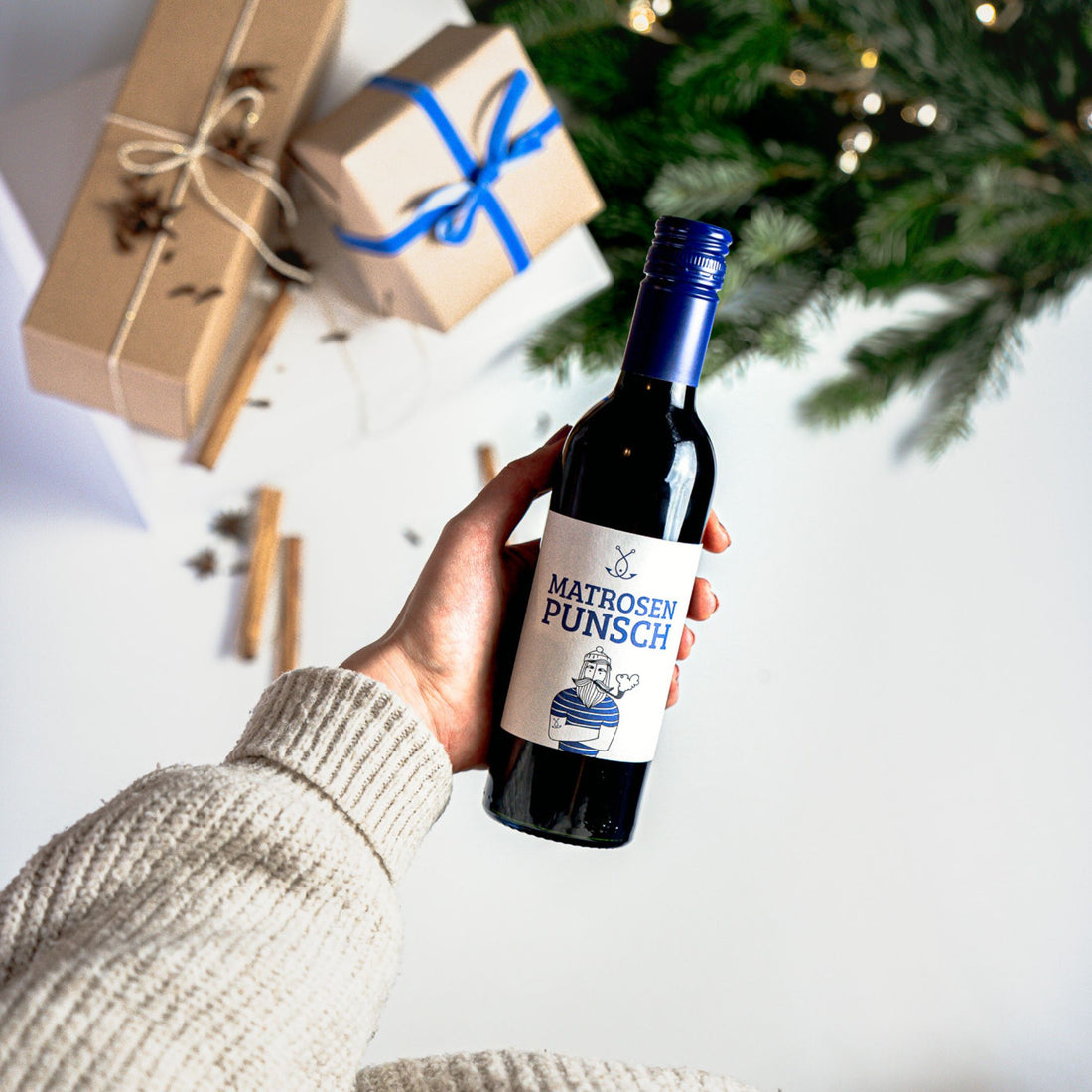 Hand hält eine Lütte Buddel Matrosenpunsch vor Weihnachtsdeko und Geschenken