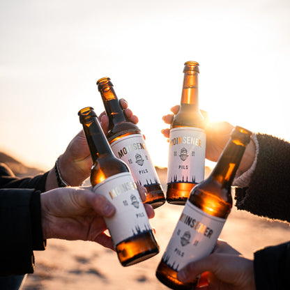 4 Moinsener Pils Bierflaschen die gemeinsam im Sonnenlicht angestoßen werden