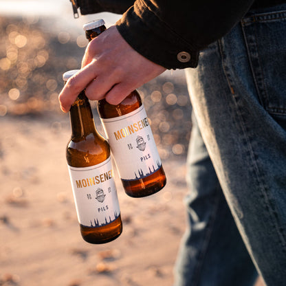 2 Moinsener Pils Bierflaschen, die von einem Mann in der Hand getragen werden