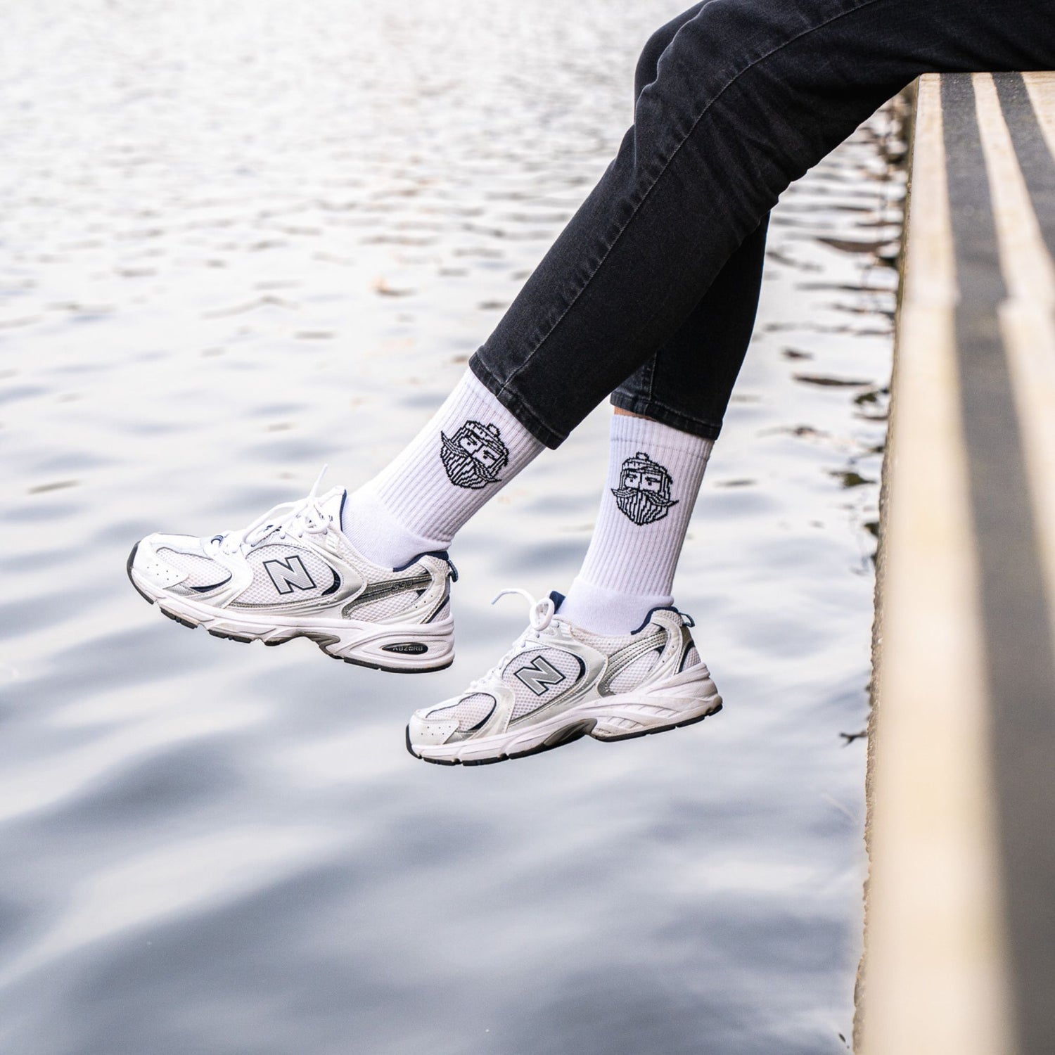 Person trägt weiße Fangfrisch Socken mit Sneakern am Wasser sitzend